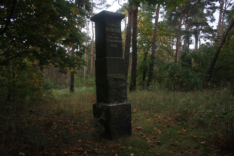 Die Vermessungsaäule steht hinter einer Wohnsiedlung.